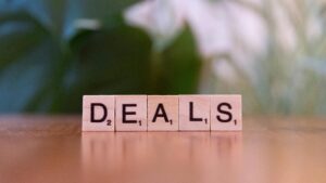 Close-up of Scrabble tiles spelling 'DEALS' on a wooden surface with blurry green background.